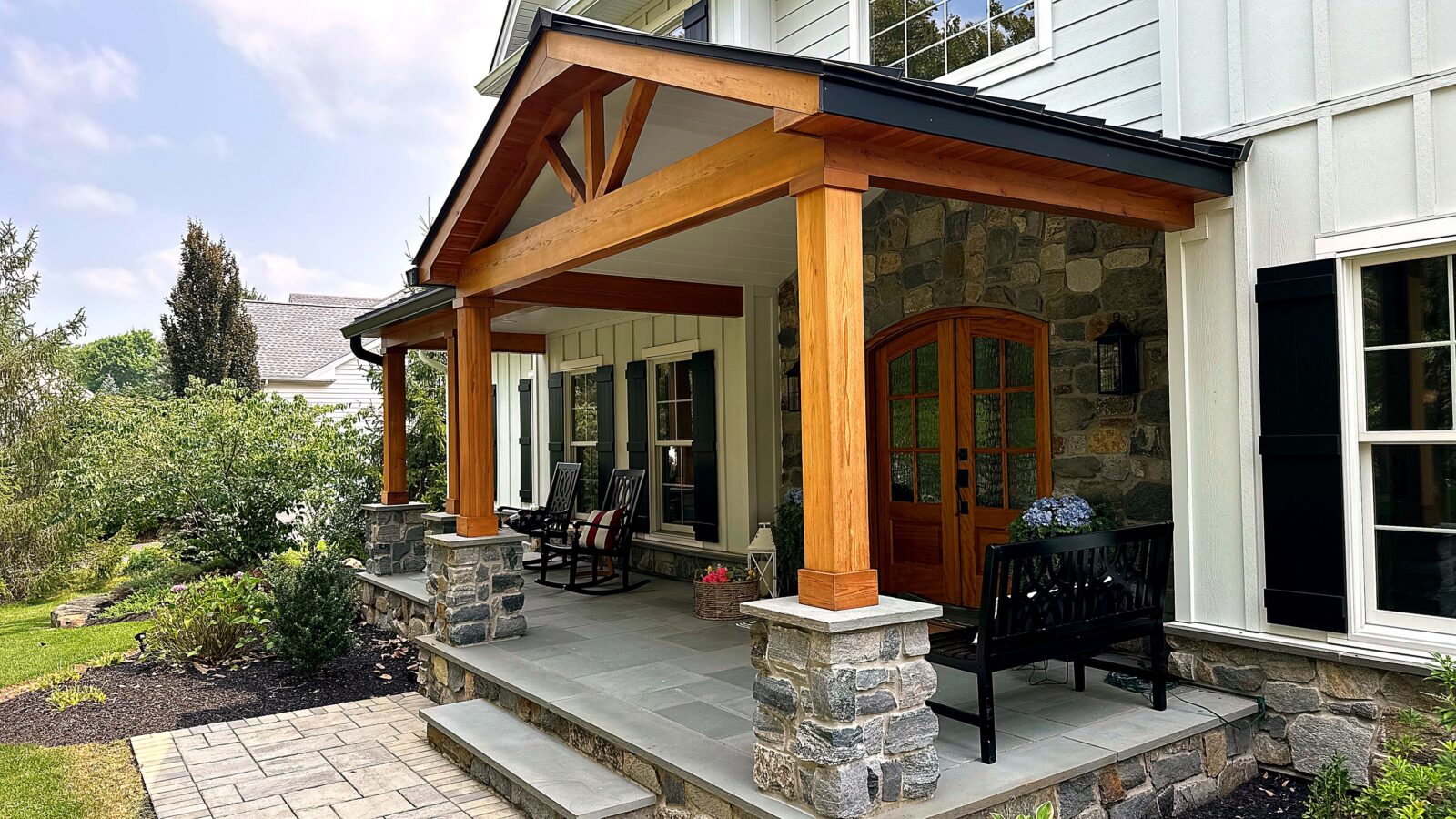 Completed front porch with timber columns, stone bases, seating and an arched double door